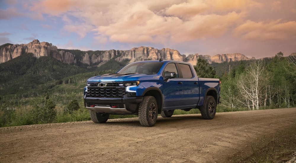 A blue 2022 Chevy Silverado 1500 ZR2 is shown from the side parked on a dirt road in the mountains at sunset.