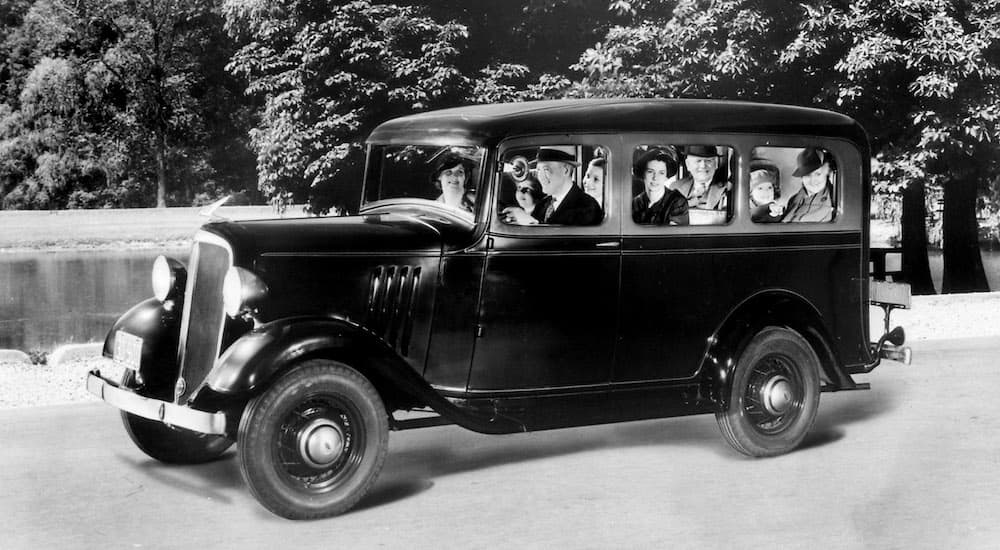 A black 1935 Chevy Suburban Carryall is shown from the side filled with a car load of people.