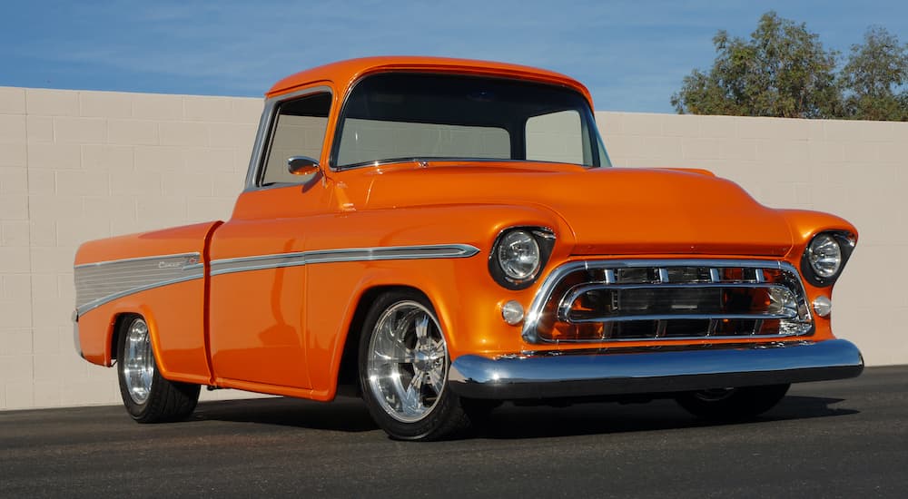 An orange 1957 Chevy Cameo is shown from the front parked in front of a cement wall after looking at a Chevy pre-order form.