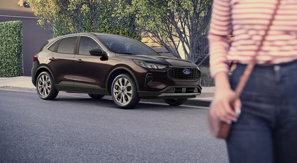 A person is shown walking away from a brown 2023 Ford Escape parked on the side of a city street.