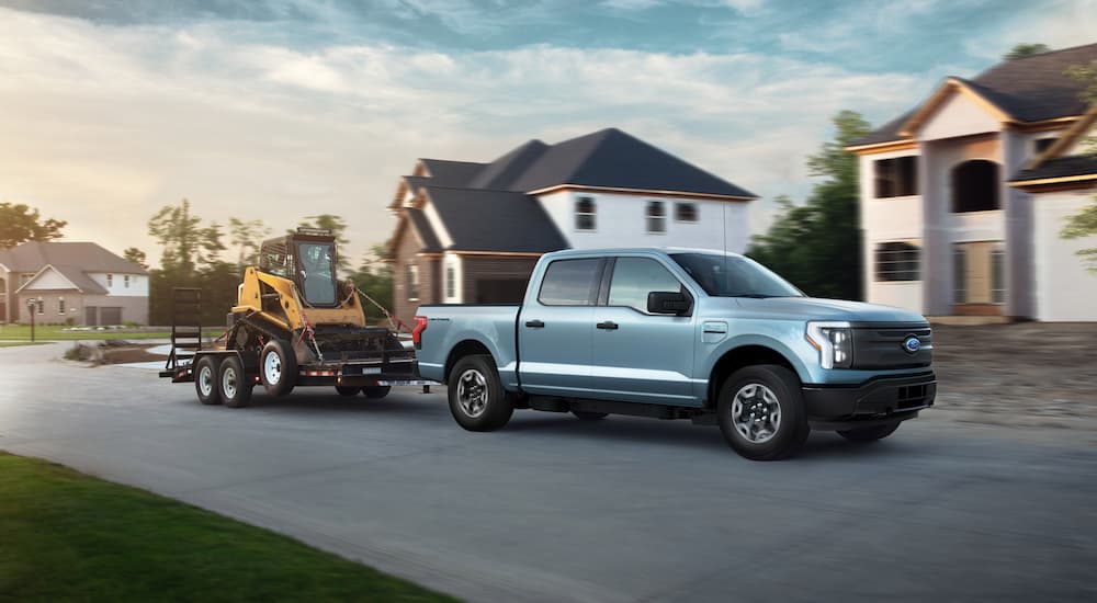 A silver 2022 Ford F-150 Lightning is shown towing heavy machinery on a trailer.