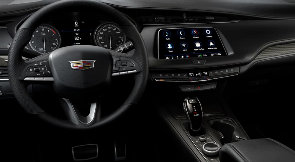 The black interior of a pre-owned luxury SUV, a 2021 Cadillac XT4, shows the steering wheel and infotainment screen.