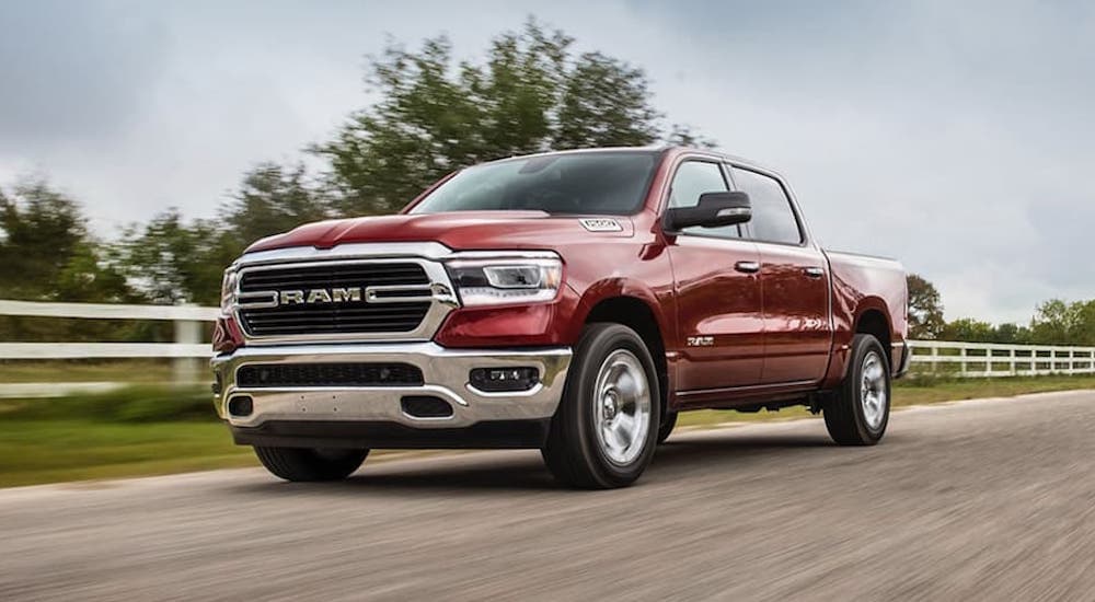 A red 2020 Ram 1500 is shown driving on a dirt road past a fence.