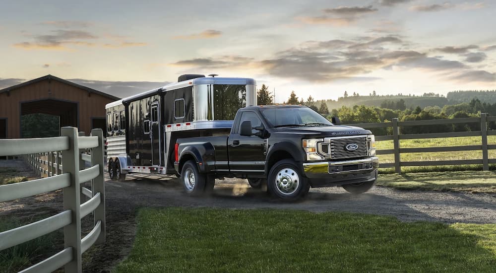 A black 2022 Ford Super Duty F-450 is shown towing a trailer on a farm.