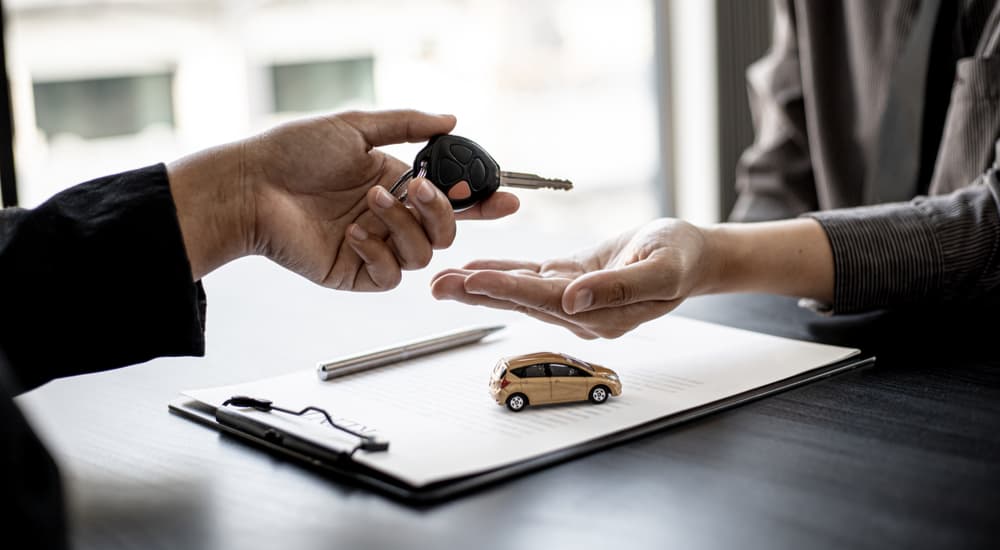 A person is shown handing a car key over to a salesman after selling their car.