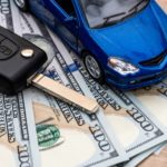 A blue toy car is shown on a stack of cash.