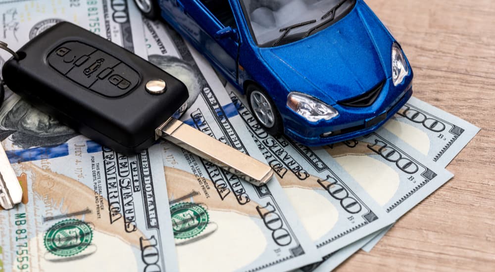 A blue toy car is shown on a stack of cash.