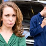 A woman is shown making a disappointed face with a mechanic in the background counting money after being scammed.