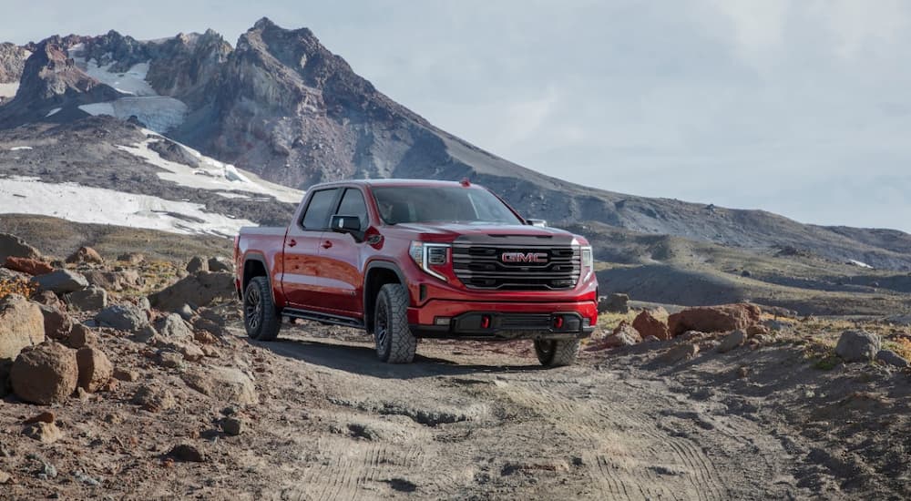 A red 2022 GMC Sierra 1500 AT4-X is shown driving on a remote dirt road.