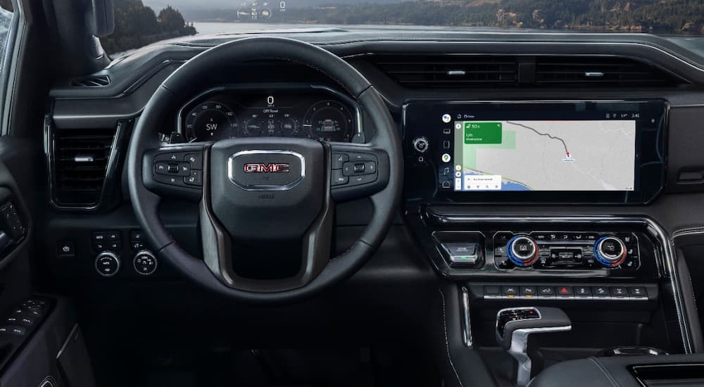 The black interior of a 2022 GMC Sierra 1500 AT4-X shows the steering wheel and infotainment screen at a truck dealership.