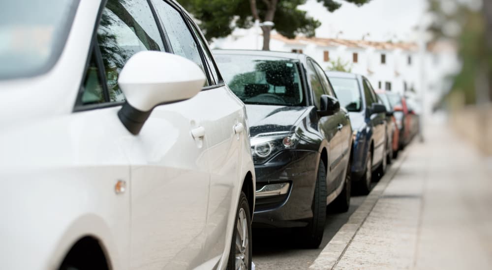 A line of used cars are shown parked on the side of a street.