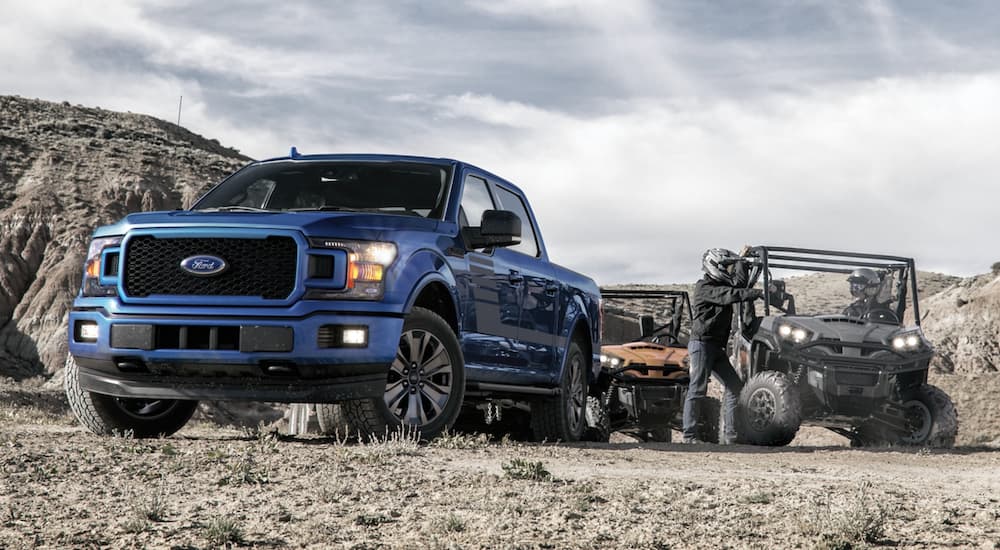 A blue 2020 Ford F-150 is shown parked in a desert area near UTVs.