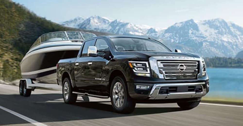 A black 2020 Nissan Titan is shown towing a boat past a body of water.