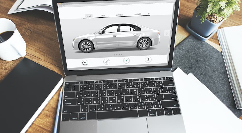 A computer searching for an online car dealer is shown in close up on a wooden table.