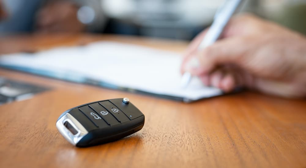 A car key is shown in close up in front of a person signing paperwork.