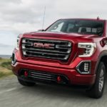 A red 2019 GMC Sierra 1500 is shown from the front driving on an open road after leaving a pre-owned GMC dealership.