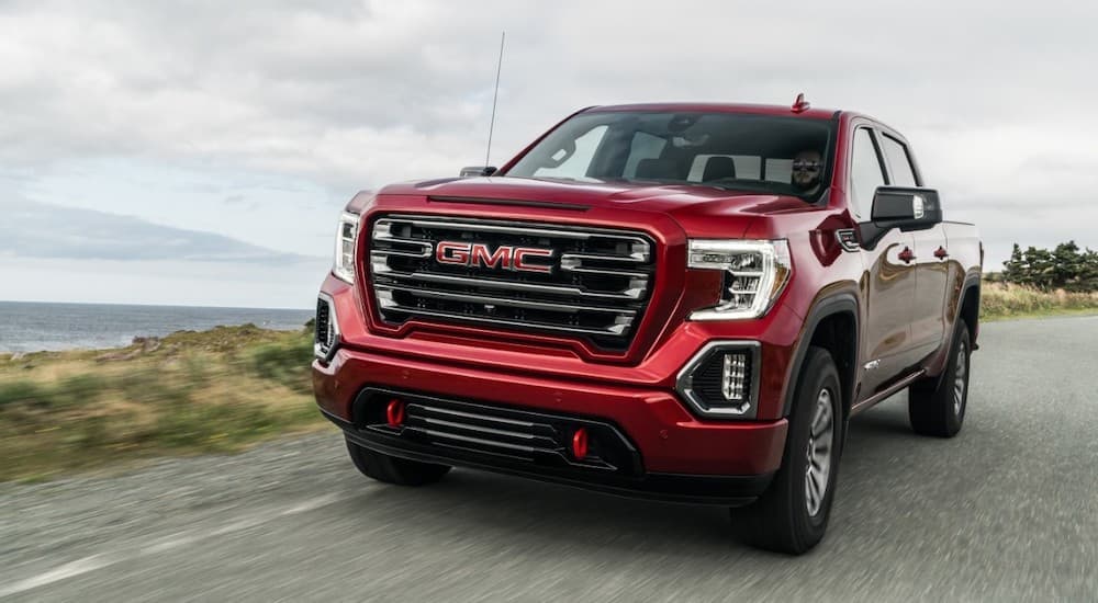 A red 2019 GMC Sierra 1500 is shown from the front driving on an open road after leaving a pre-owned GMC dealership.