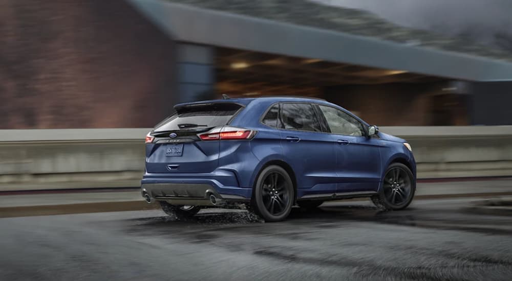 A blue 2022 Ford Edge is shown from the side driving on an open road in the rain.