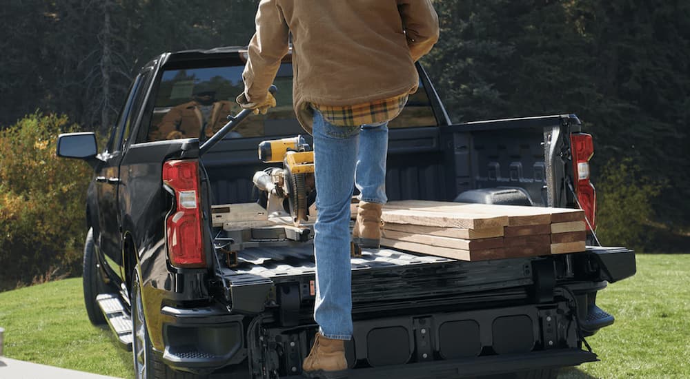 The rear of a black 2022 Chevy Silverado 1500 Limited is shown as a person loads the truck with wood and tools. 