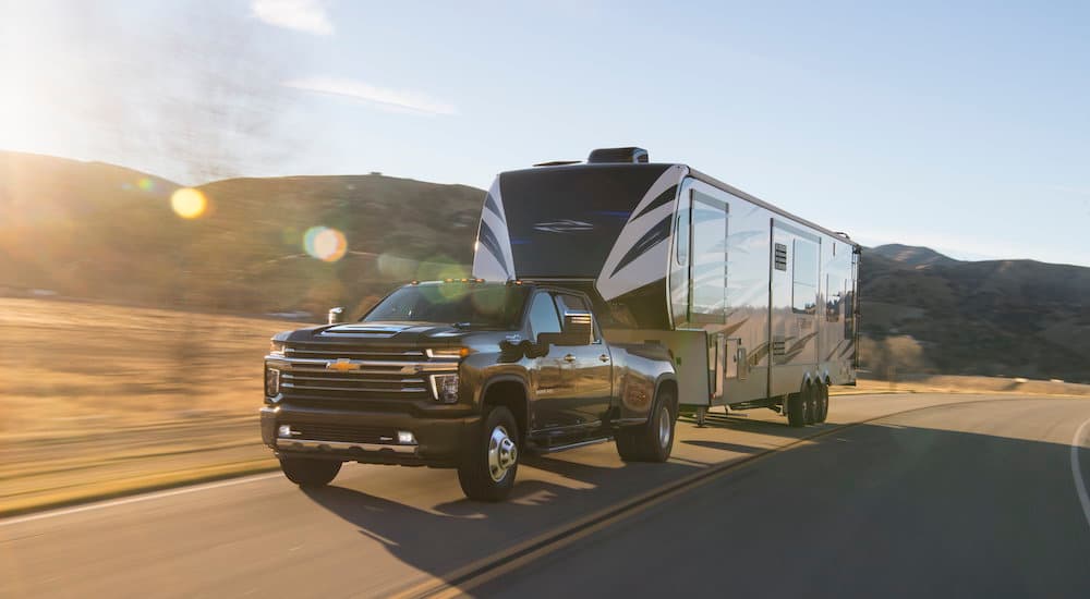 A black 2022 Chevy Silverado 3500 HD is shown towing a large trailer on a highway. 