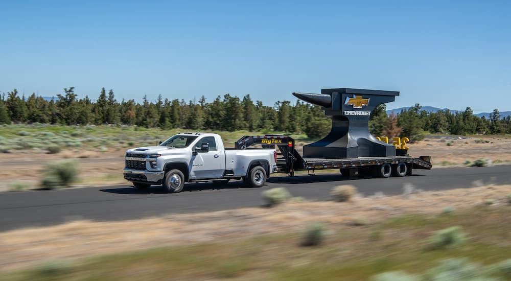 A white 2022 Chevy Silverado 3500 HD is shown towing a gooseneck trailer with a large anvil.