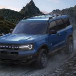 A blue 2022 Ford Bronco Sport is shown from the side driving on a dirt path in the mountains.