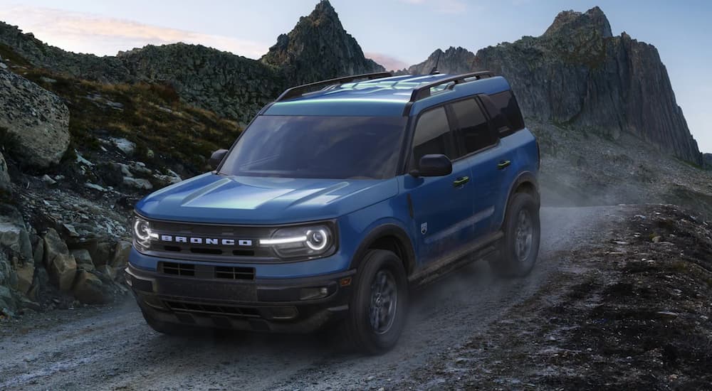 A blue 2022 Ford Bronco Sport is shown from the side driving on a dirt path in the mountains.