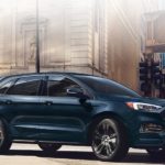 A dark blue 2022 Ford Edge ST is shown from the side driving through a city.