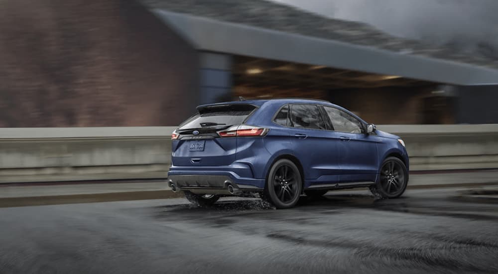 A blue 2020 Ford Edge is shown from the rear driving on an open road in the rain after winning a 2022 Ford Edge vs 2022 Hyundai Santa Fe comparison.