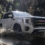 A white 2022 GMC Yukon AT4 is shown off-roading through a river.