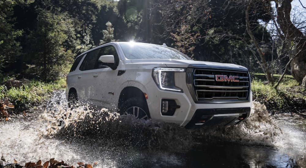 A white 2022 GMC Yukon AT4 is shown off-roading through a river.