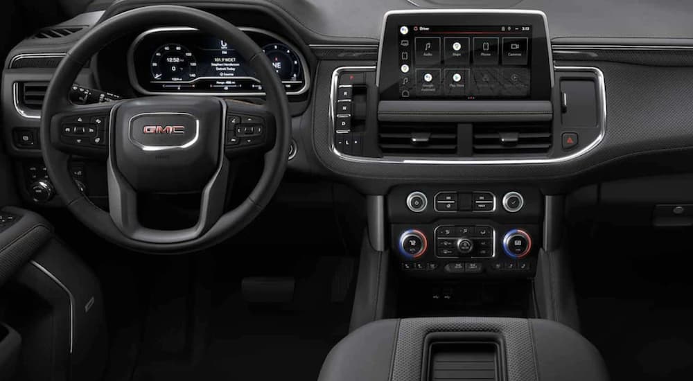 The black interior of a 2022 GMC Yukon shows the steering wheel and infotainment screen.