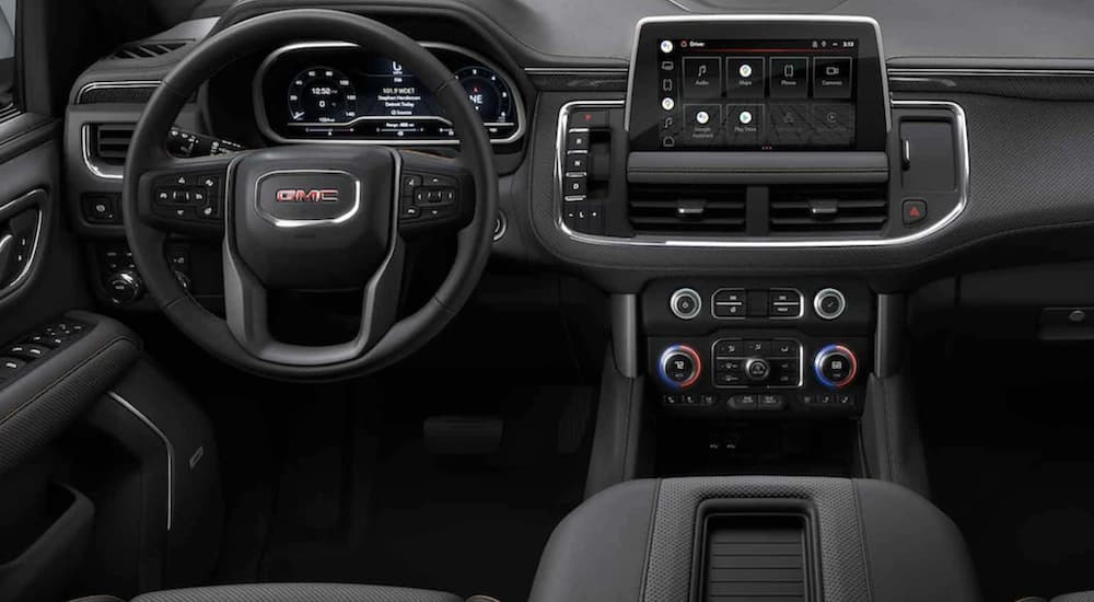 The black interior of a 2022 GMC Yukon shows the steering wheel and infotainment screen.