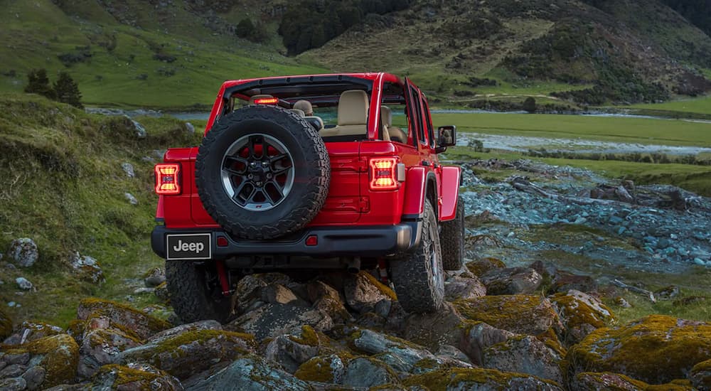 A red 2022 Jeep Wrangler Rubicon is shown from the rear off-roading on a rocky path.