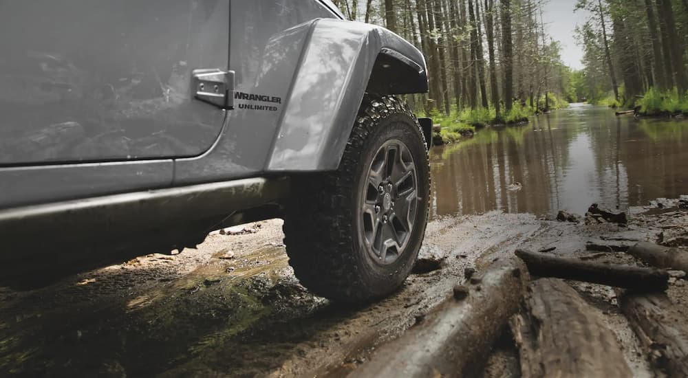 A close up of the side and tire of a silver 2022 Jeep Wrangler Unlimited is shown off-roading.