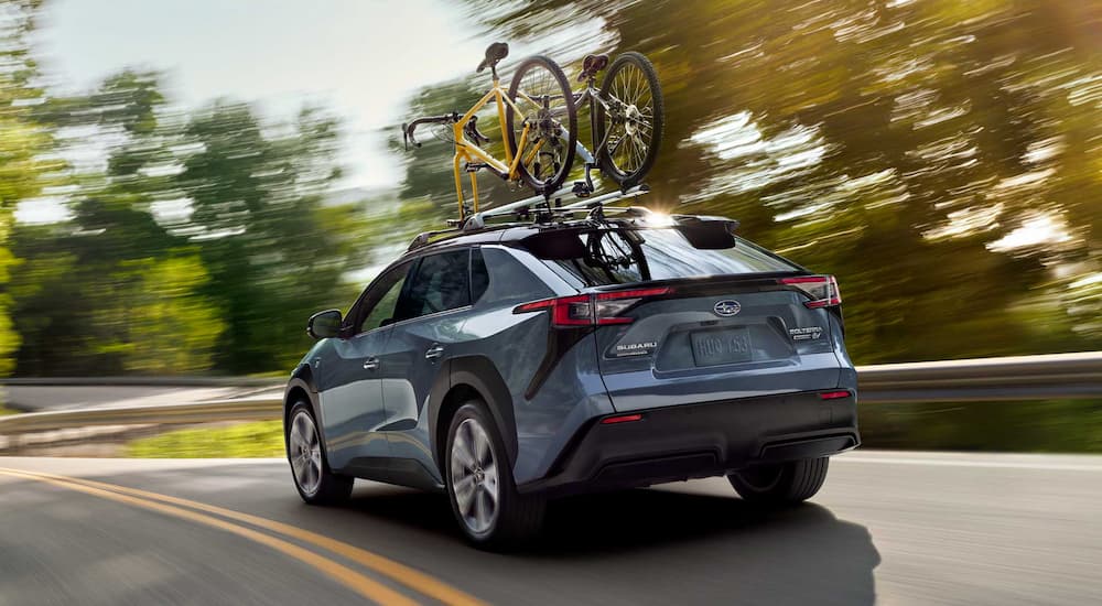 A blue 2023 Subaru Solterra is shown from a rear angle with two bikes on the roof rack.