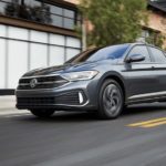 A grey 2022 Volkswagen Jetta SEL is shown from the side driving on an open road through a city.