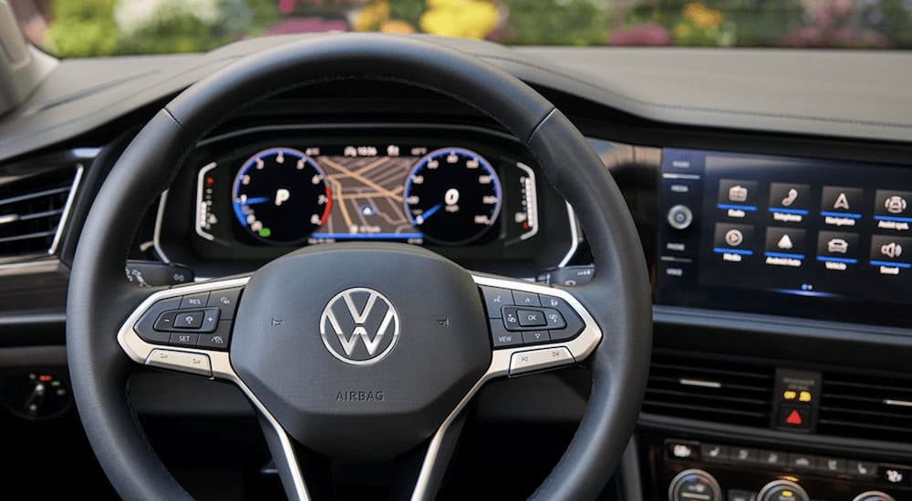 The black interior of a 2022 Volkswagen Jetta SEL shows the steering wheel and infotainment screen.