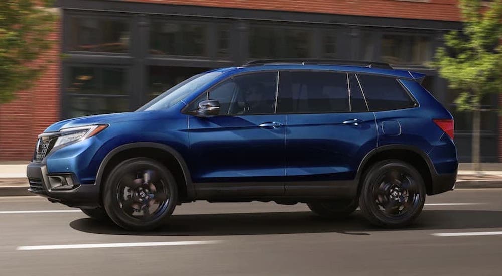 A blue 2022 Honda Passport is shown from the side driving down a city street.
