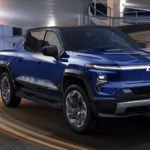 A blue 2024 Chevy Silverado EV is shown from the front driving through a parking garage.