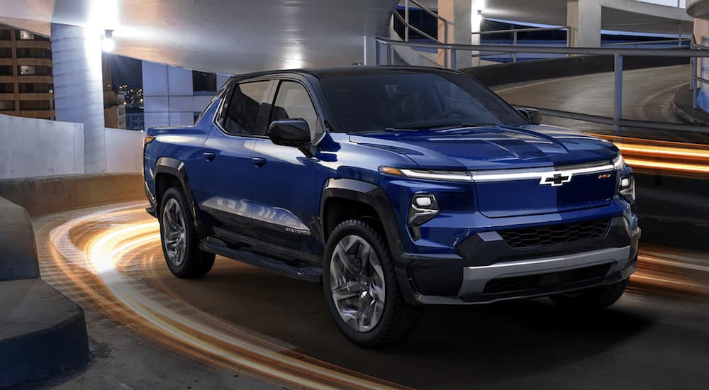 A blue 2024 Chevy Silverado EV is shown from the front driving through a parking garage.