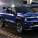 A blue 2024 Chevy Silverado EV is shown from the side driving on an open road.