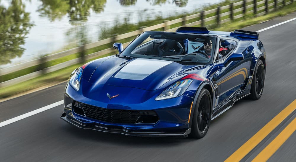 A blue 2018 Chevy Corvette GrandSport is shown from the front driving on an open road past a body of water.