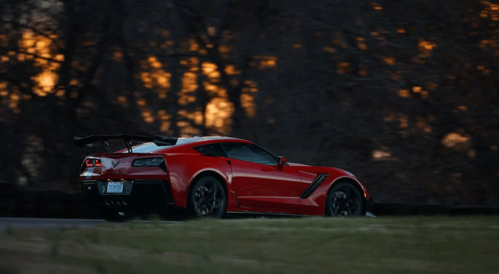 A red 2019 Chevy Corvette ZR1 is shown from the side driving on a tree lined road at sunset.