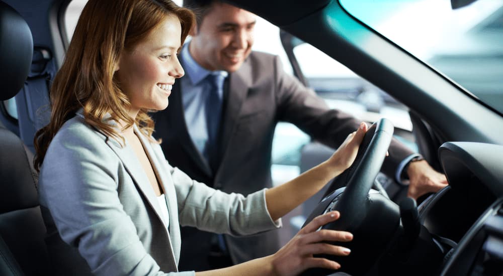 A person is shown sitting in the drivers seat of a car at a Certified Pre-Owned Ford dealer.