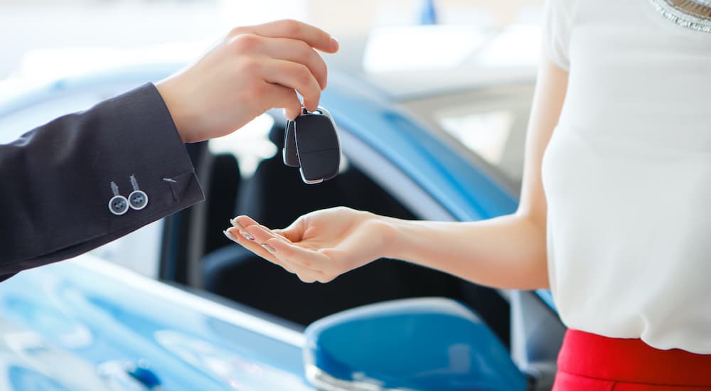 A salesperson is shown passing a car key to a person a Certified Pre-Owned GMC dealer.