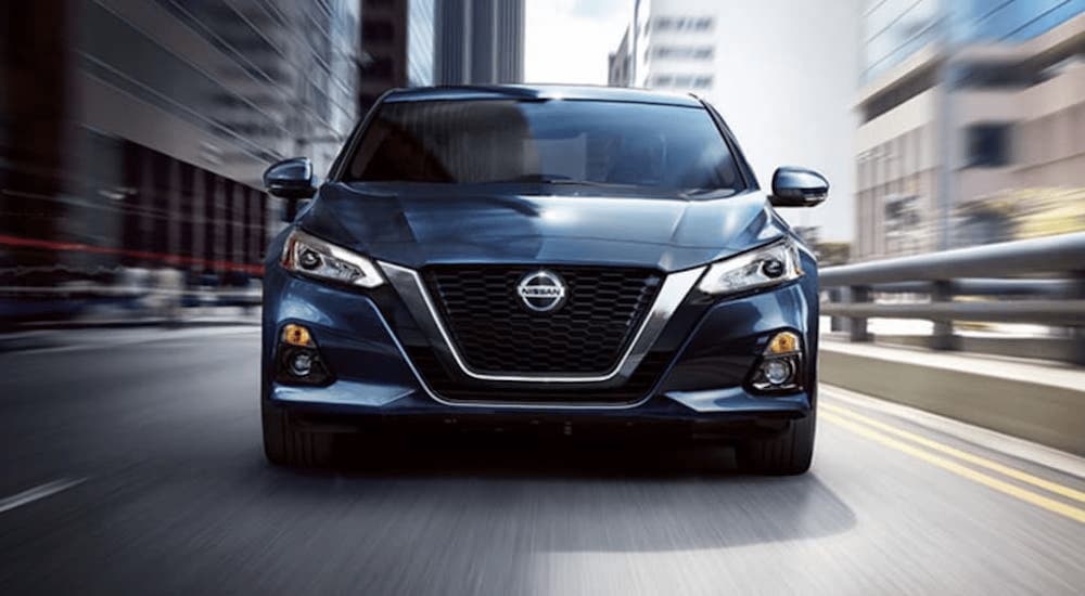 A blue 2020 Nissan Altima is shown from the front driving through a city after leaving a Certified Pre-Owned Nissan dealer.