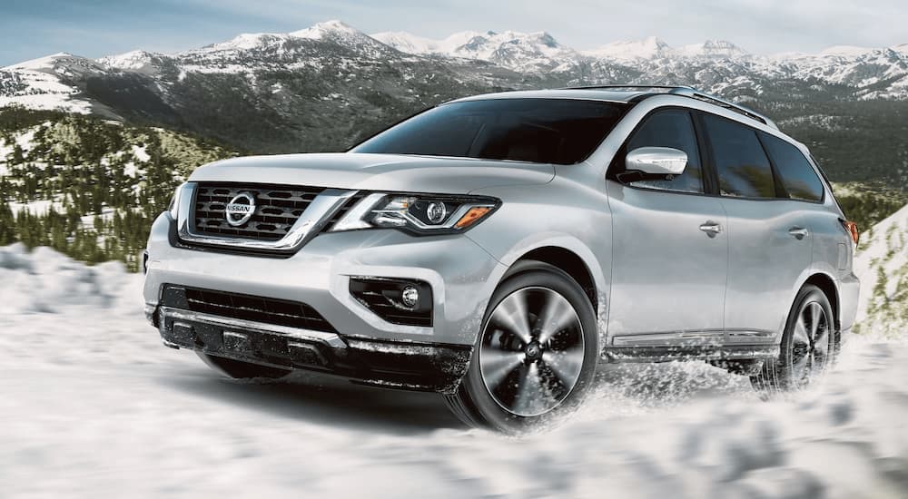 A white 2020 Nissan Pathfinder is shown from the side driving through snow.