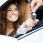 A person is shown smiling as someone passes them a key at a dealership with Certified Pre-Owned cars for sale.