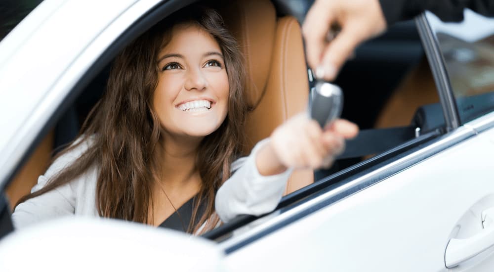 A person is shown smiling as someone passes them a key at a dealership with Certified Pre-Owned cars for sale.